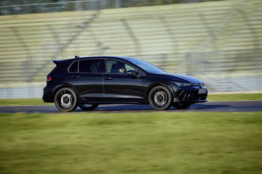 Zwarte Volkswagen Golf rijdt op het circuit, zijaanzicht met dynamische achtergrond.