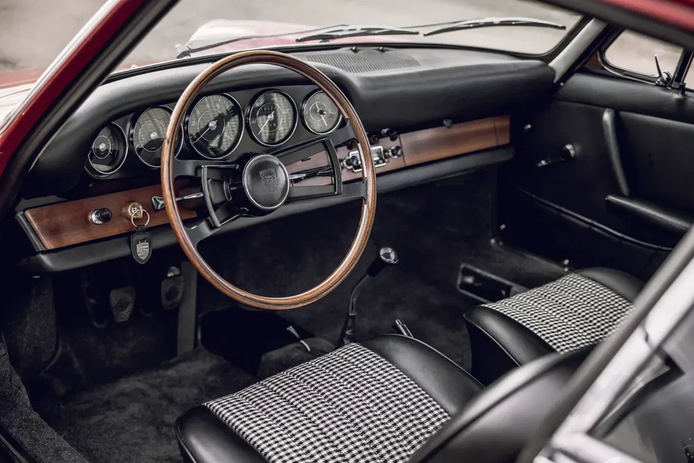 Vintage interieur van een klassieke Porsche 911 met houten stuur en geruite stoelen.