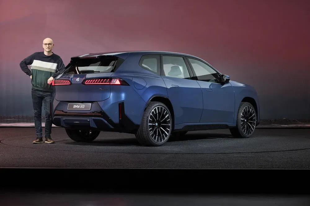 Man poseert met blauwe BMW iX3 onder stijlvolle binnenverlichting.