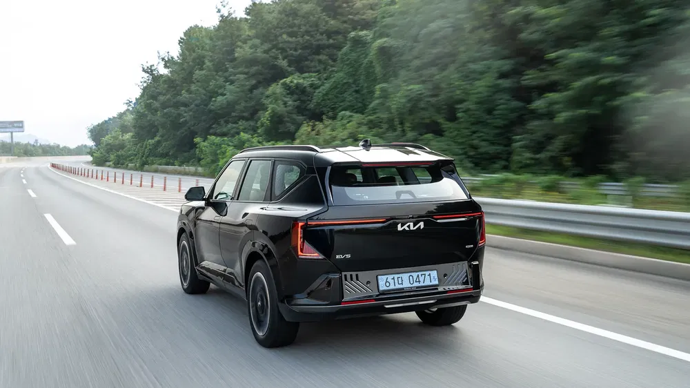 Kia EV5 noir roulant sur une autoroute bordée d'arbres, design moderne et aérodynamique.