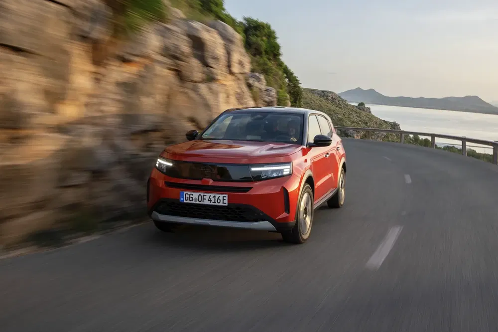 SUV rouge électrique sur une route côtière sinueuse, Opel Mokka en mouvement rapide.