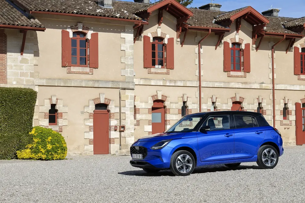 Blauwe MG3 auto voor een historisch stenen gebouw met rode ramen.