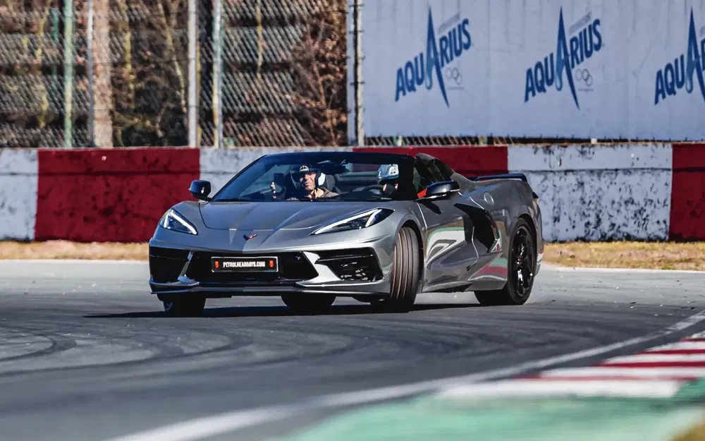 Grijze Chevrolet Corvette C8 in bocht op racecircuit, dynamisch en sportief.