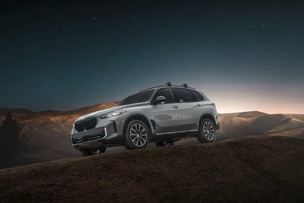 {"fr":"SUV BMW X5 argenté sur colline au crépuscule, montagnes en arrière-plan.","nl":"Zilveren BMW X5 SUV op heuvel bij schemering, bergen op de achtergrond."}