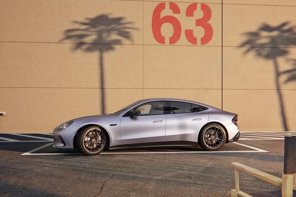 Zilveren Mercedes-AMG GT 63 geparkeerd voor een beige muur met palmbomenschaduwen.