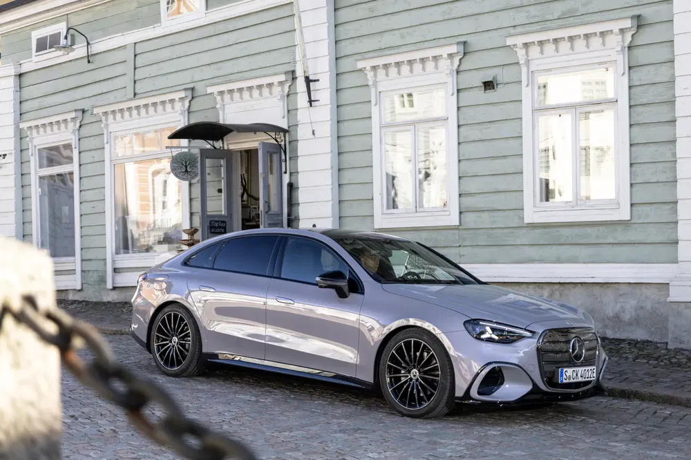 Grijze Mercedes-Benz sedan geparkeerd voor houten huis, moderne en elegante stijl.