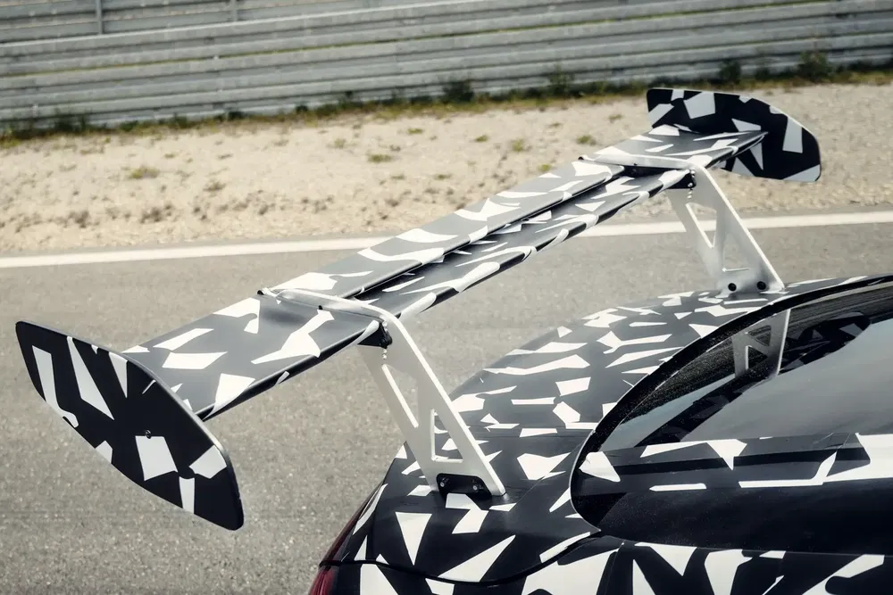 {"fr":"Aileron arrière camouflage sur prototype de voiture sportive, améliorant l'aérodynamisme sur piste.","nl":"Achterspoiler met camouflage op sportwagenprototype, verbetert aerodynamica op circuit."}