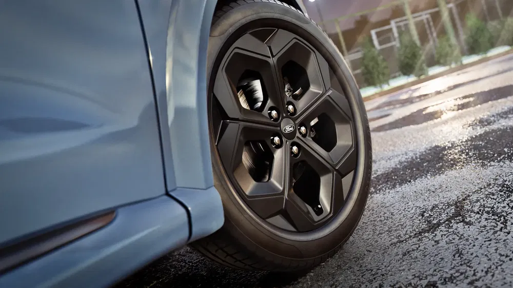 Close-up van Ford lichtmetalen velg met glanzend zwart, blauwe auto geparkeerd.