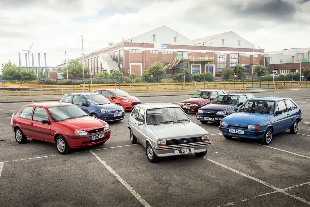 Collection de Ford Fiesta vintage et modernes garées devant un bâtiment industriel.