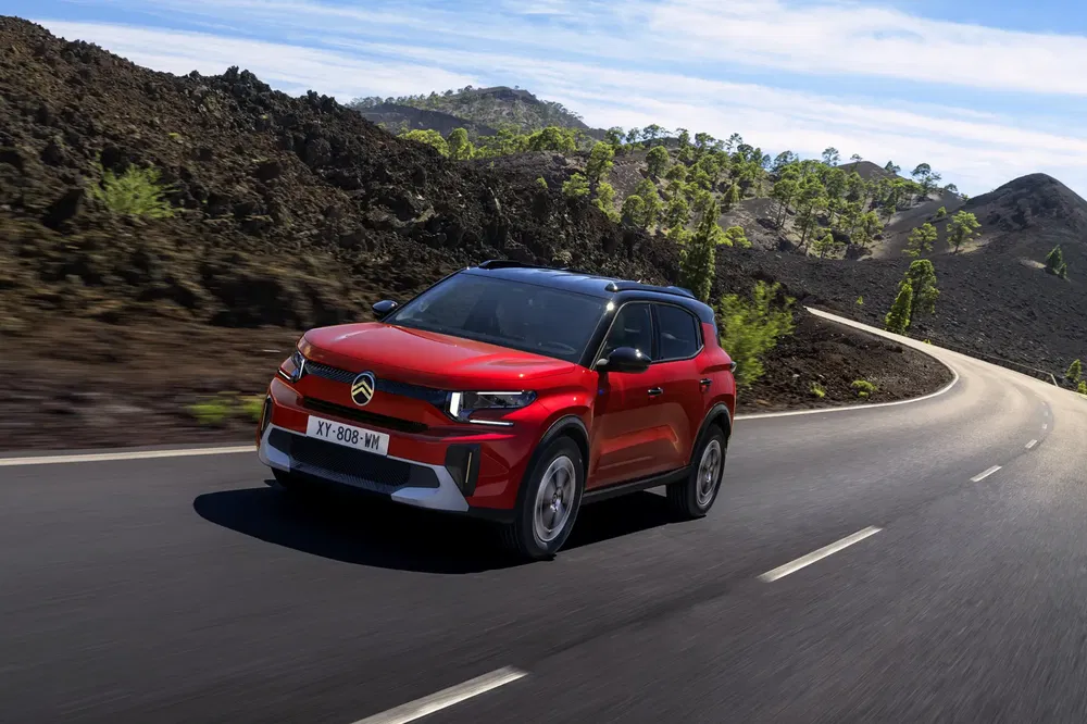 Rode Citroën C3 Aircross op kronkelige weg met vulkanisch landschap op de achtergrond.