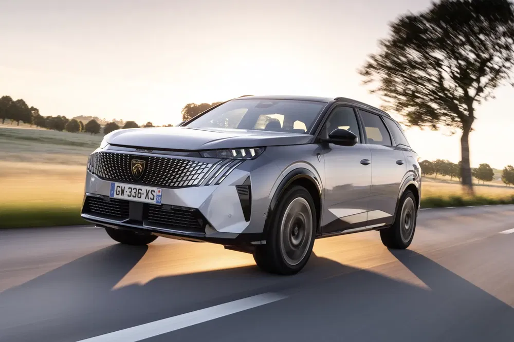 SUV Peugeot moderne roulant sur route ensoleillée avec paysage de campagne à l'arrière-plan.