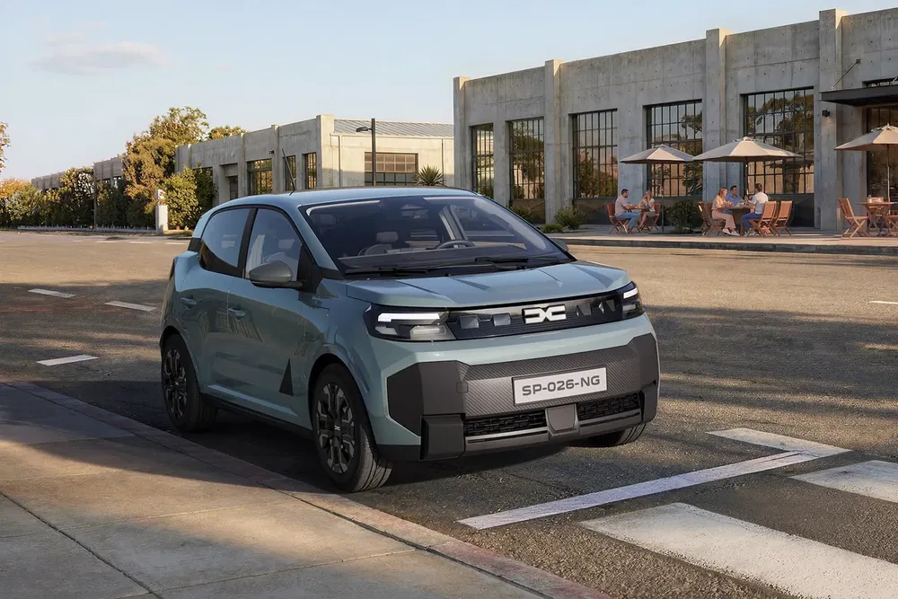 Voiture électrique Dacia Spring sur une rue ensoleillée près d'un café moderne.