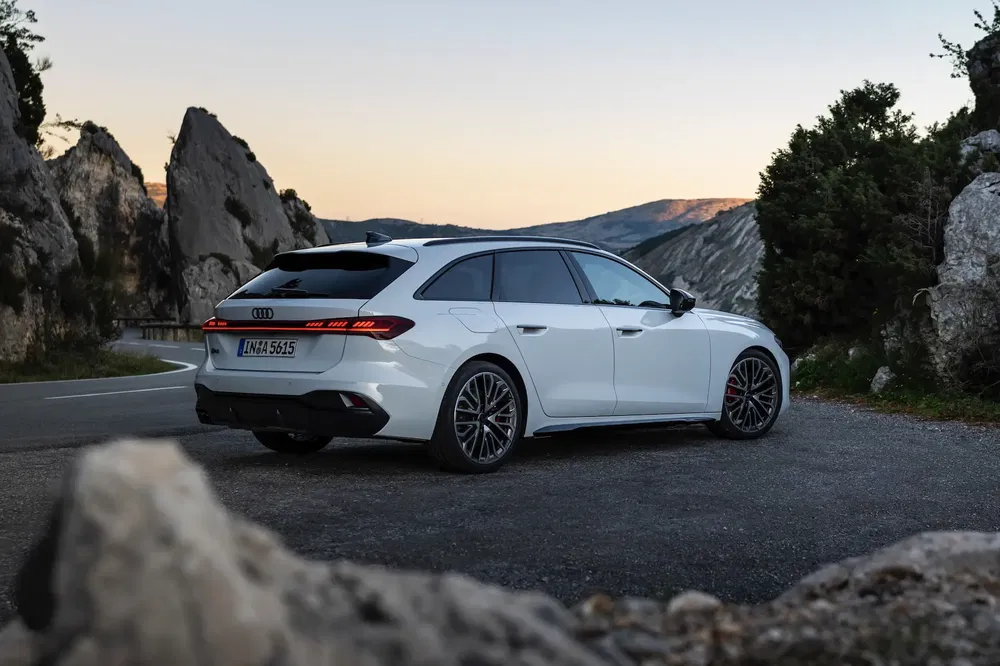 Audi blanche sur route de montagne au coucher du soleil, paysage pittoresque.