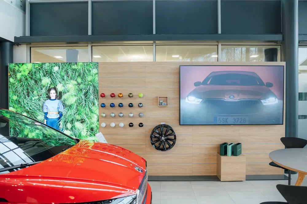 Salle d'exposition avec Skoda orange, échantillons de peinture et affiches promotionnelles.