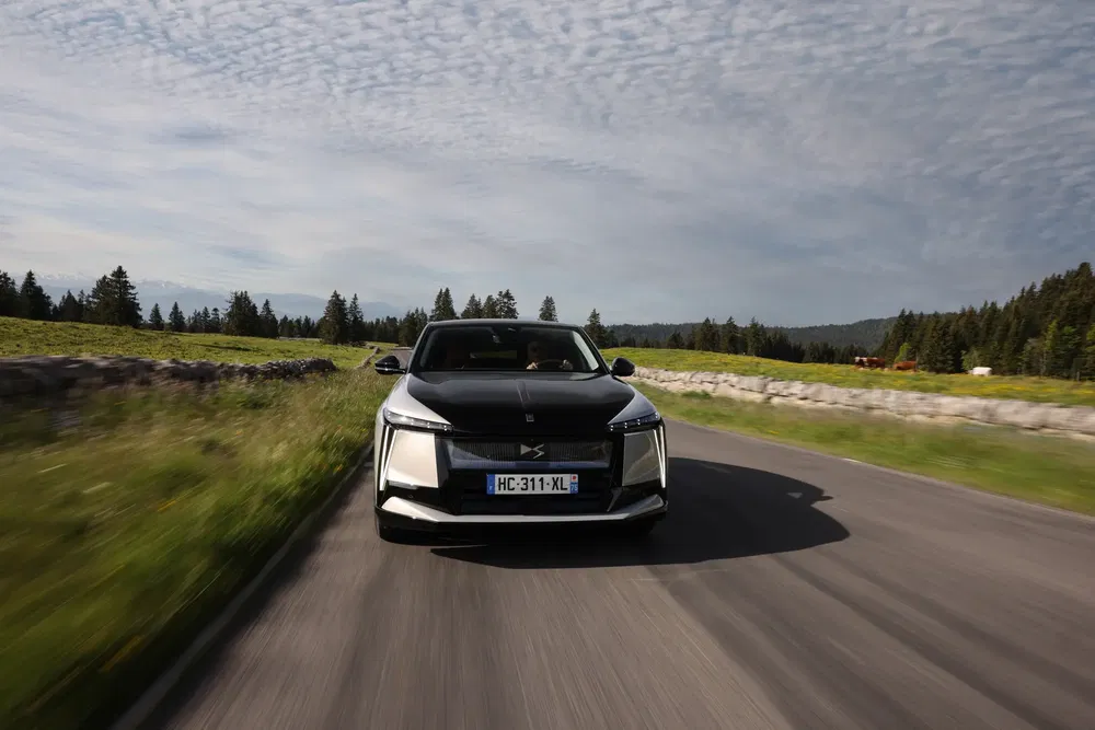 Zwarte DS 4 E-Tense rijdt op landweg, met bewolkte lucht op de achtergrond.