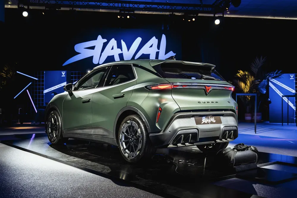 Groene Cupra Tavascan SUV tijdens introductie, moderne podiumverlichting en achtergrondpaneel.