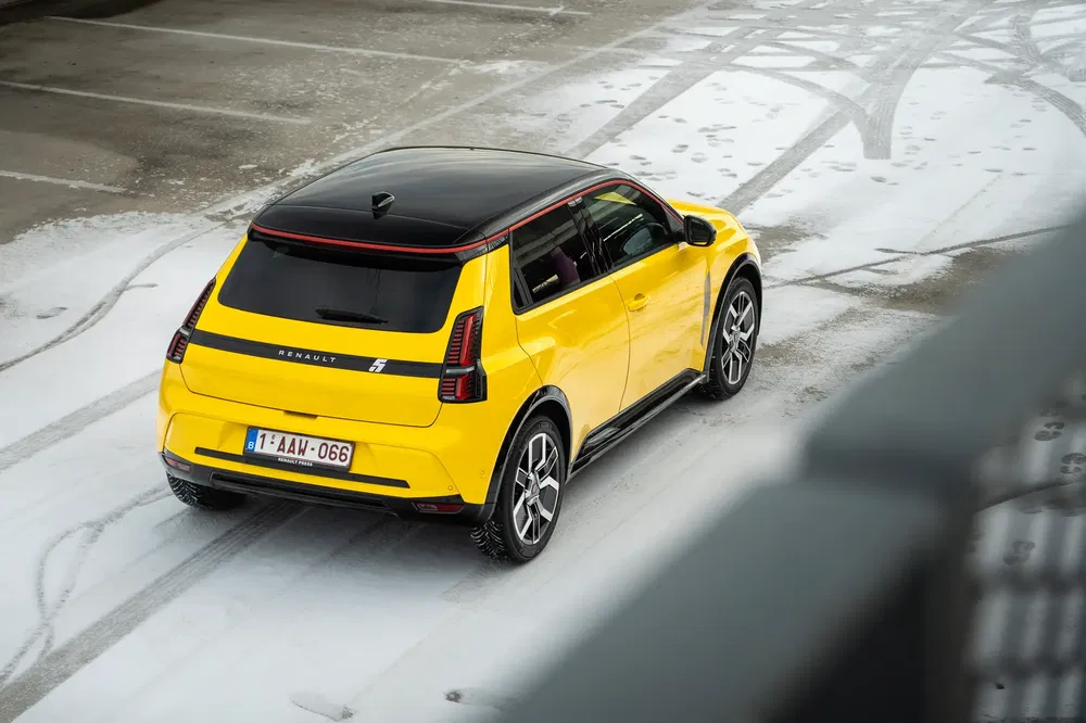 Renault 5 électrique jaune sur route enneigée, vue arrière trois-quarts.