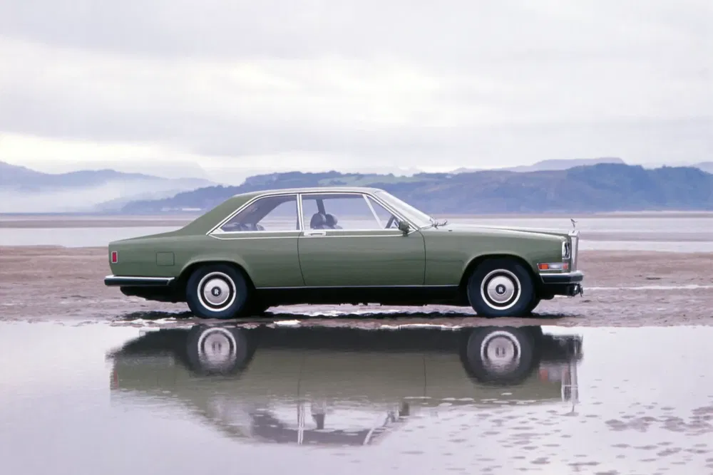 {"fr":"Voiture vintage verte sur une plage avec reflet dans l'eau, paysage montagneux en arrière-plan.","nl":"Groene vintage auto op strand met waterreflectie, bergachtig landschap op de achtergrond."}