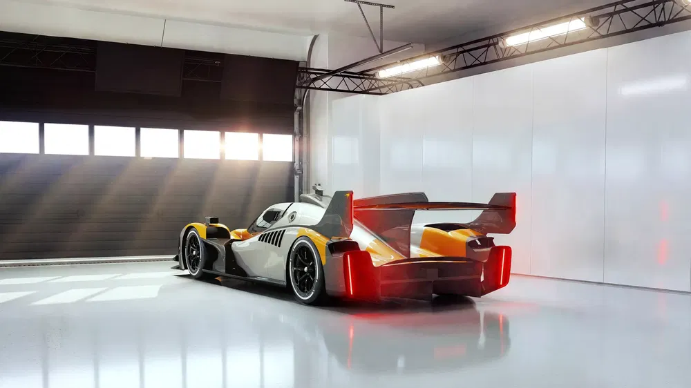 Voiture de course moderne avec aileron arrière imposant dans un garage bien éclairé.