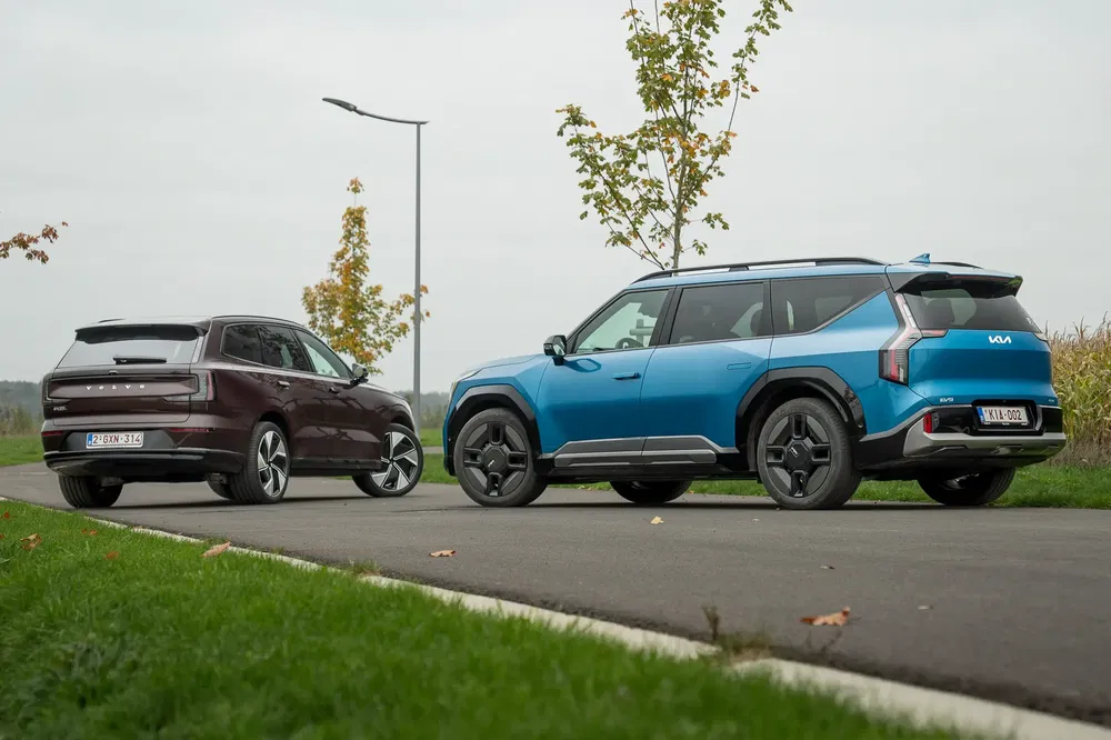 Kia SUV bleu et voiture marron sur route de campagne, ciel nuageux.