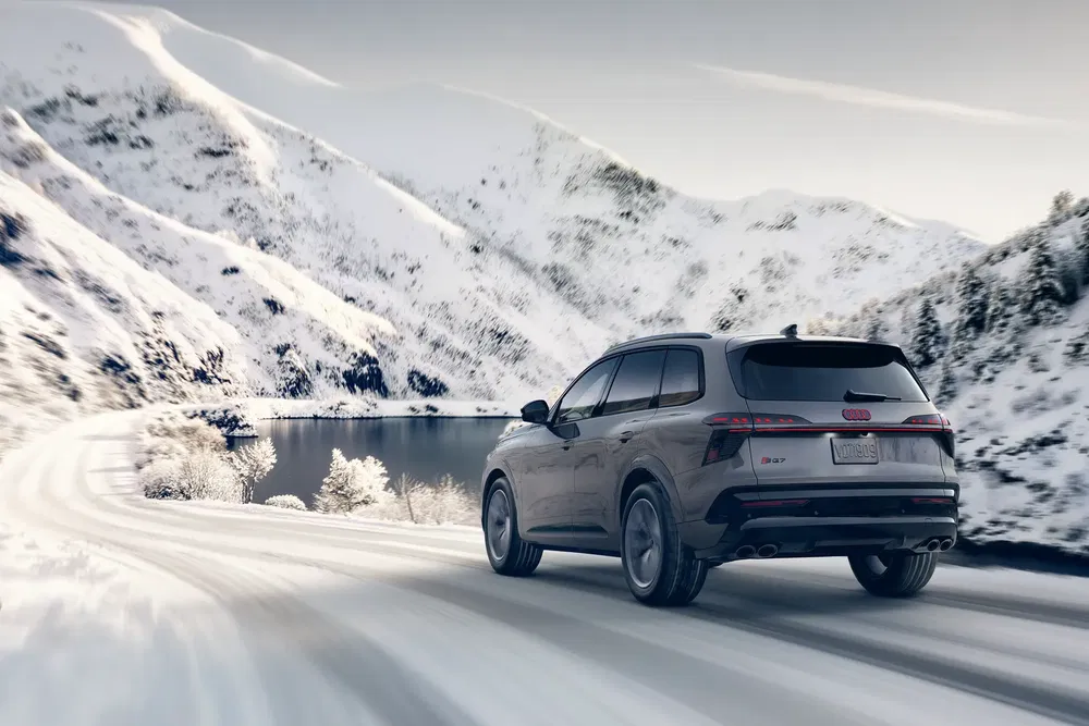 Audi Q5 roulant sur route enneigée avec montagnes en arrière-plan.