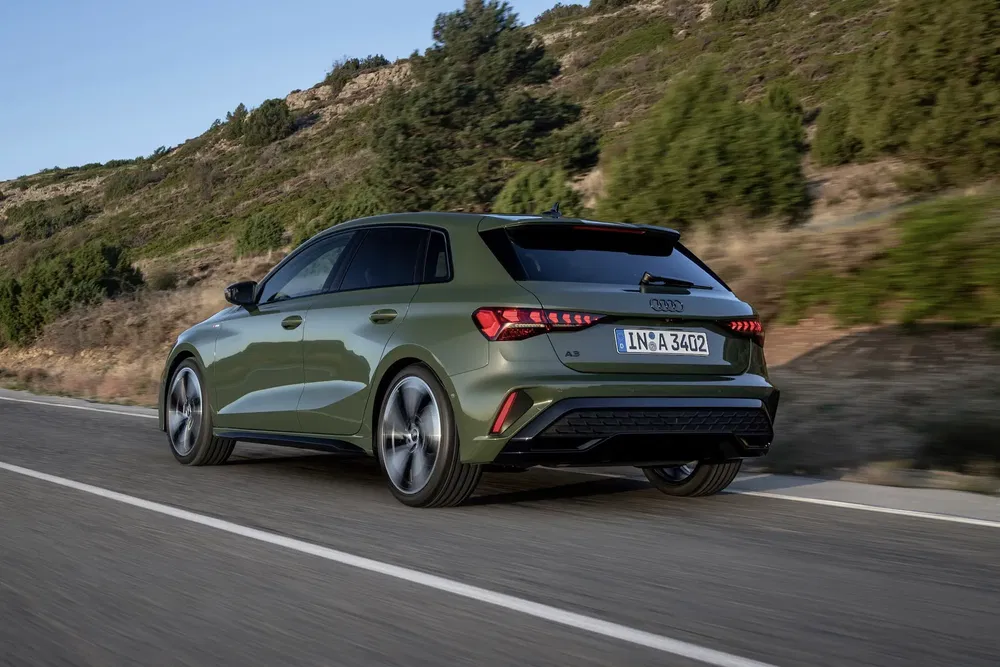 Audi A3 verte roulant sur une route sinueuse entourée de paysages naturels.