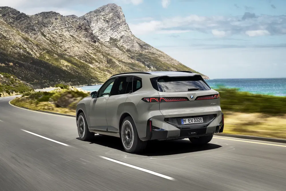 BMW iX roulant sur une route côtière avec vue sur la mer et montagnes.