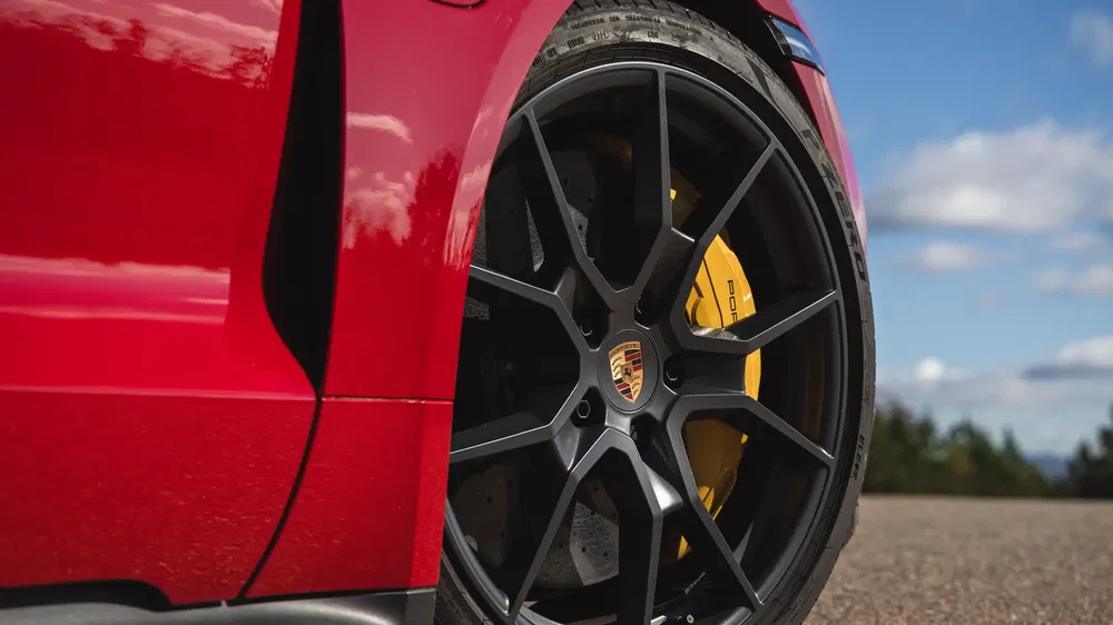 Gros plan d'une roue Porsche en alliage noir avec étrier de frein jaune sur une voiture rouge.
