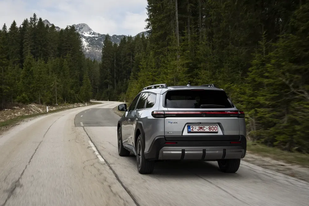 Toyota bZ4X gris roulant sur route de montagne bordée d'arbres verts.
