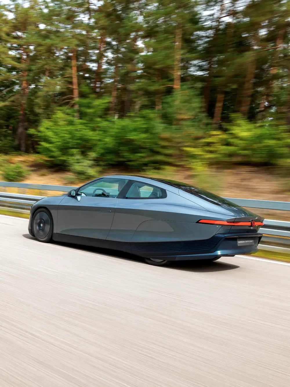 Voiture électrique Mission R en mouvement rapide sur une route bordée d'arbres.