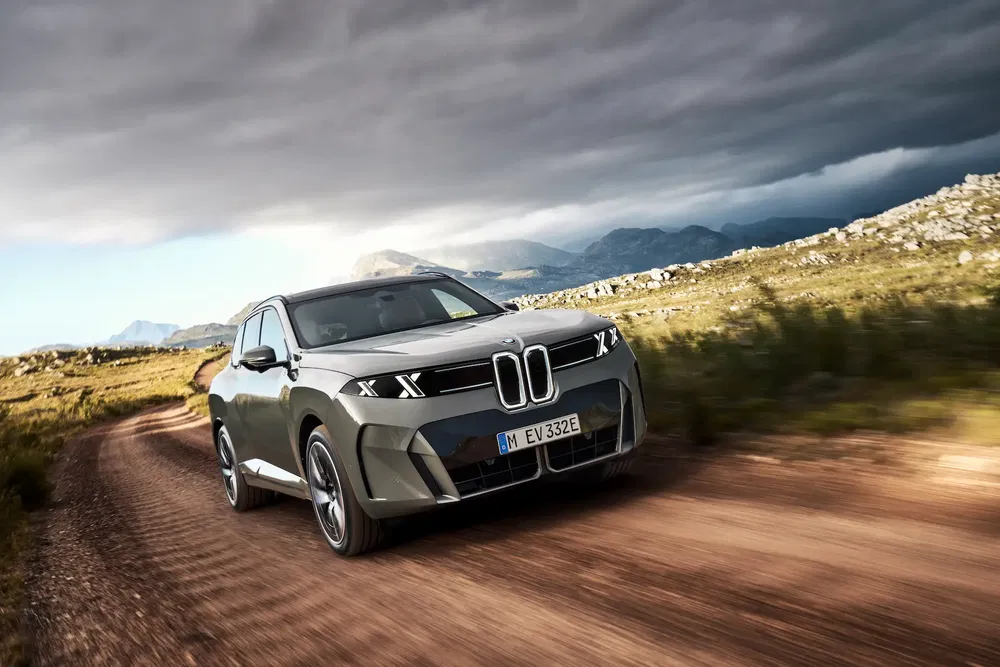 BMW électrique sur route montagneuse, sous ciel nuageux et paysage dramatique.