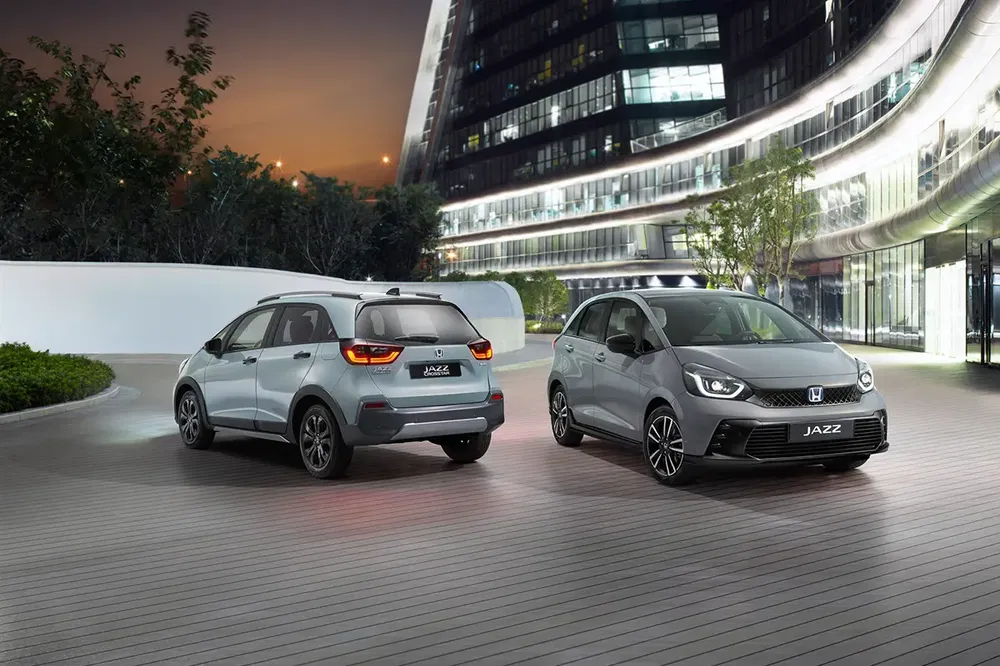 Twee grijze Honda Jazz auto's geparkeerd voor een modern gebouw bij schemering.