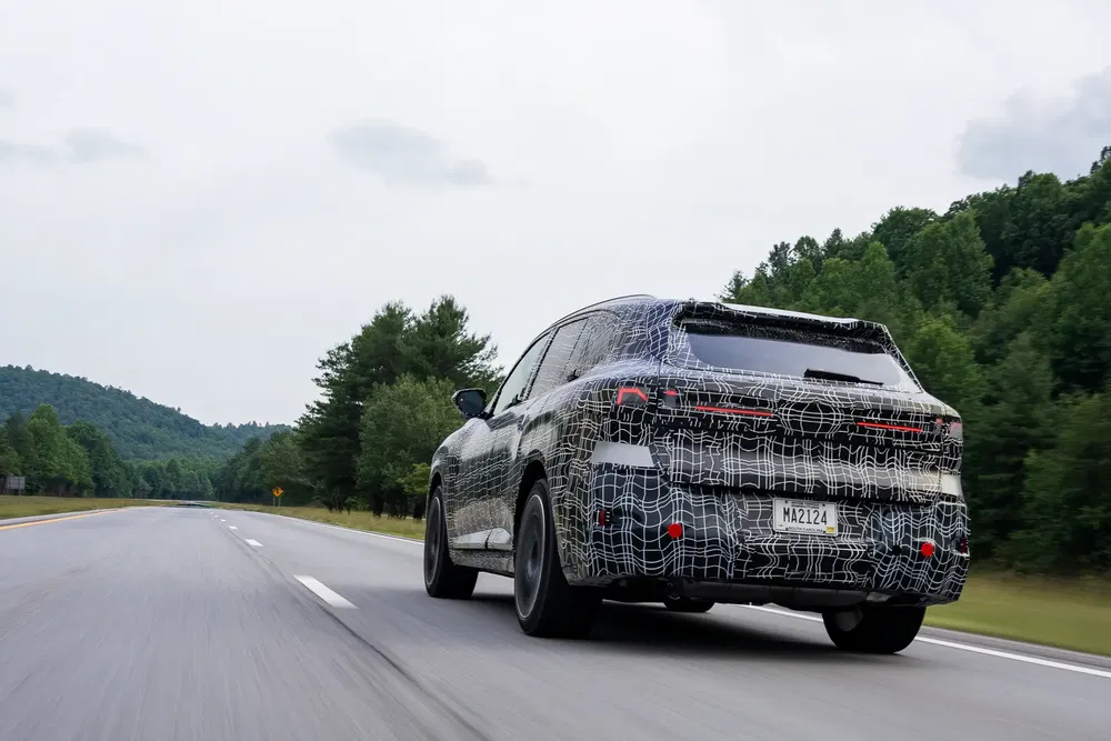 Geëxcamoufleerde BMW SUV op de weg, omgeven door groene bossen.