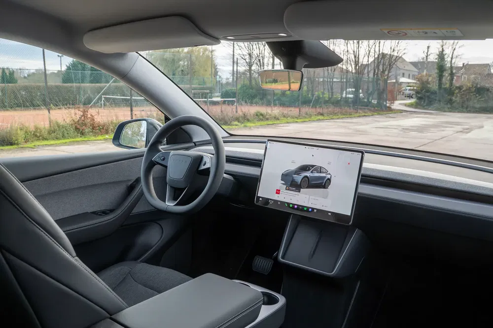 Modern interieur Tesla met centraal touchscreen en minimalistisch stuurwiel, geparkeerd buiten.