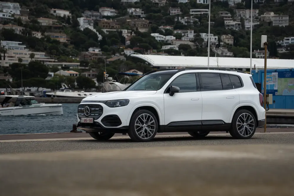 SUV Mercedes-Benz GLB blanc stationné près d'un port avec des yachts en arrière-plan.