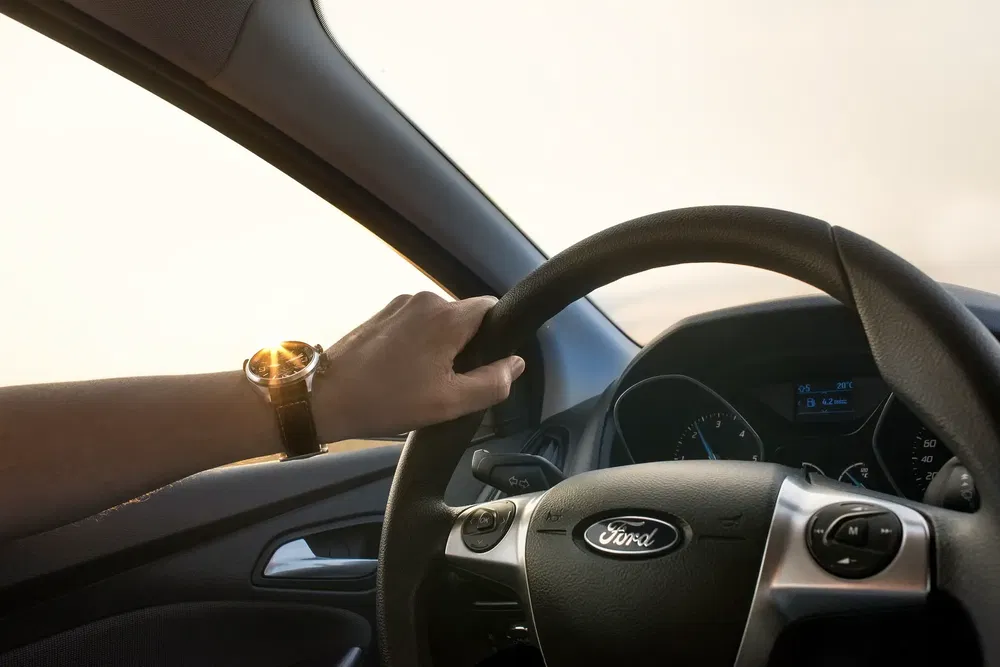 Main sur le volant d'une Ford, conducteur portant une montre-bracelet élégante.