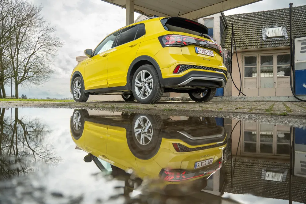 Gele Volkswagen T-Cross weerspiegeld in een plas bij een vintage tankstation.