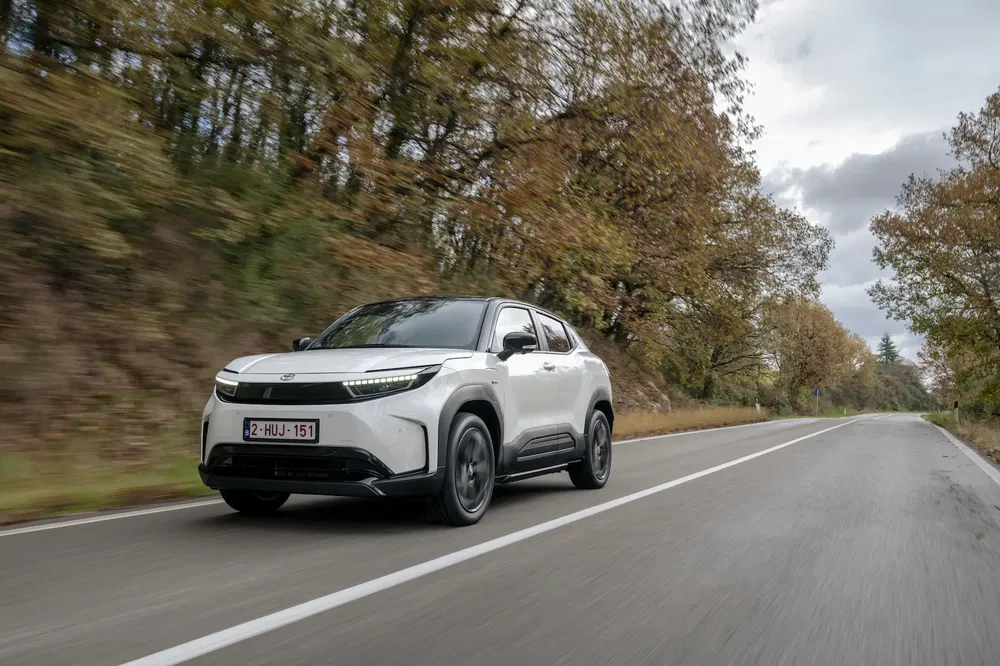Toyota bZ4X blanc roulant sur une route bordée d'arbres à l'automne.