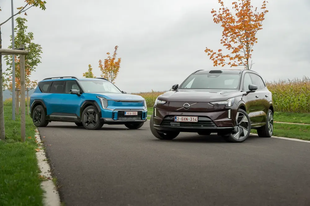 SUV Kia EV9 bleu et SUV Volvo EX90 marron sur route automnale.
