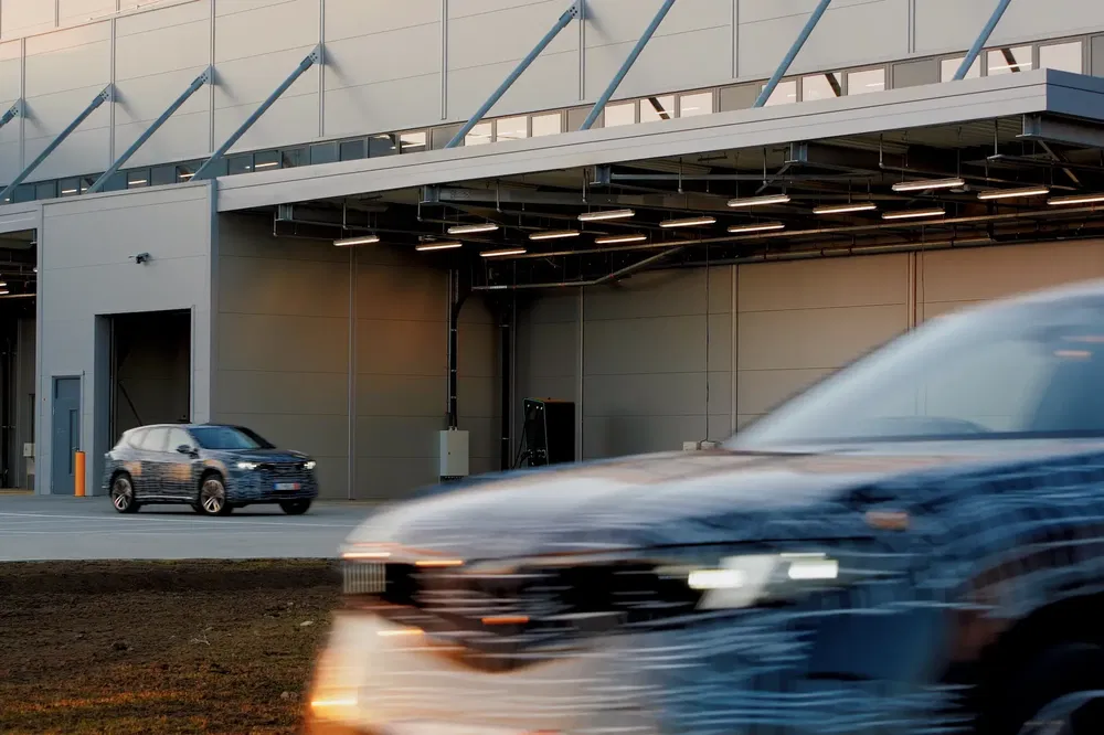Voiture camouflée en test près d'un bâtiment industriel moderne.