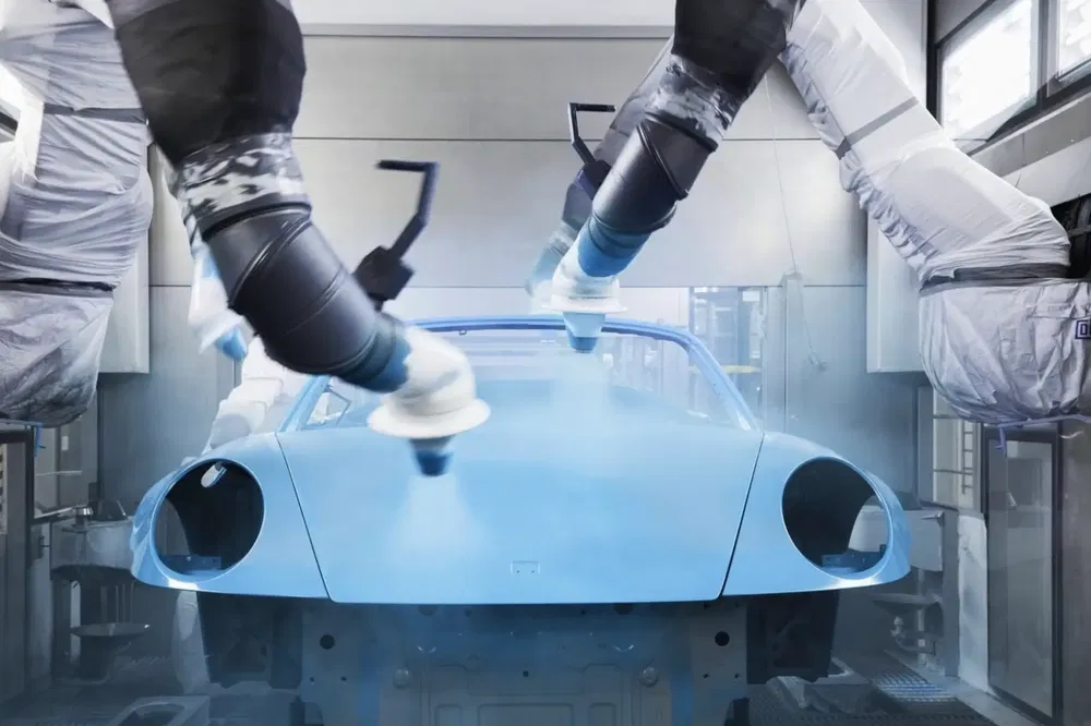 Robots peignant une carrosserie de voiture bleue dans une usine automobile moderne.