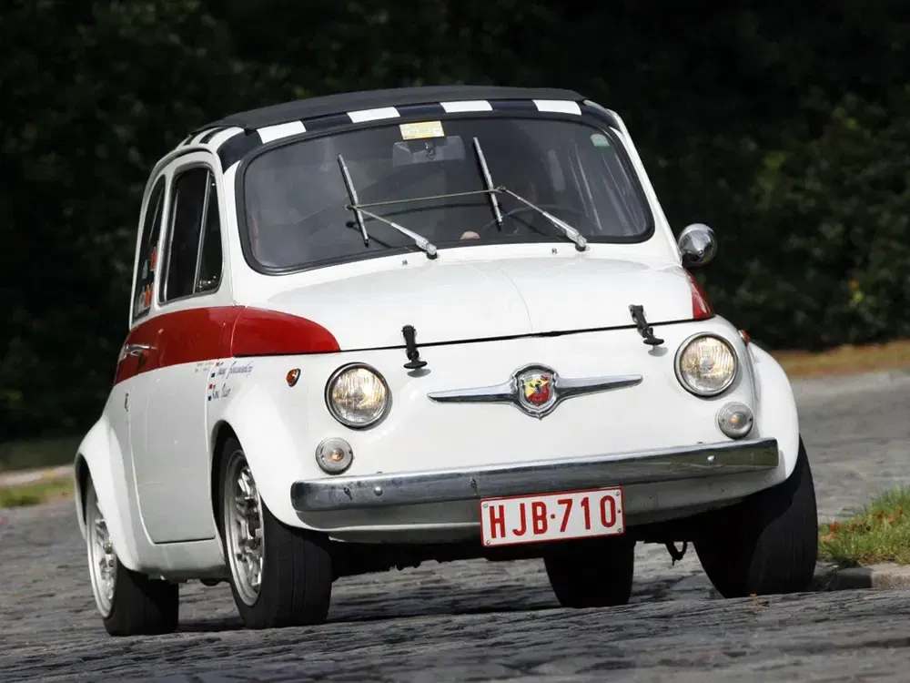 Klassieke Fiat 500 met Belgische nummerplaat HJB-710, rijdend op kasseienweg.