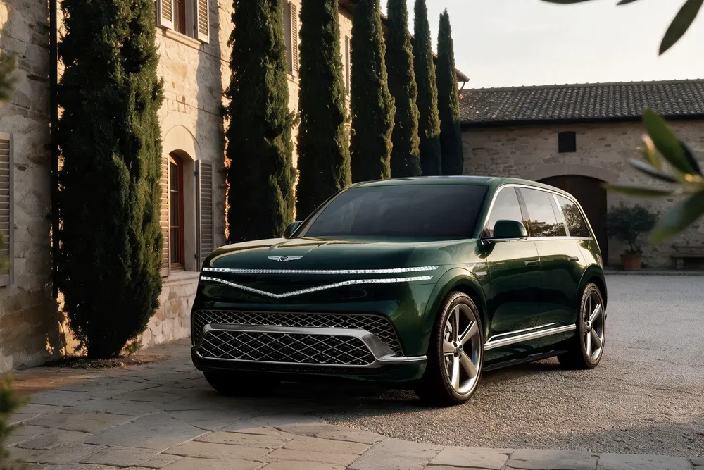 Genesis GV80 SUV vert devant un manoir en pierres, entouré de cyprès élancés.