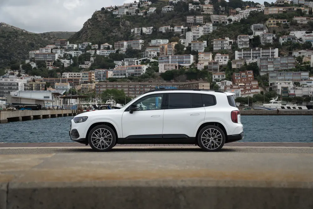 Mercedes-Benz GLB blanc sur fond de port avec colline et bâtiments résidentiels.
