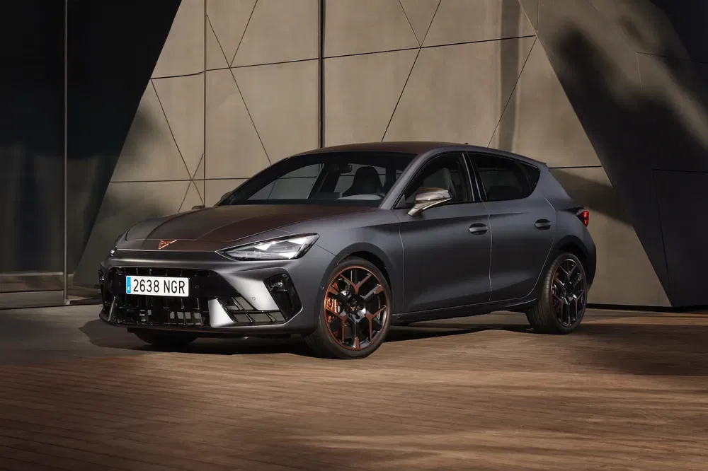 Grijze Cupra hatchback met lichtmetalen velgen tegen moderne betonnen achtergrond.