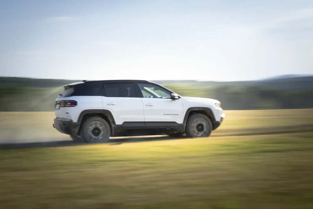 Jeep Compass blanche en mouvement rapide sur un chemin de terre dans un paysage champêtre.