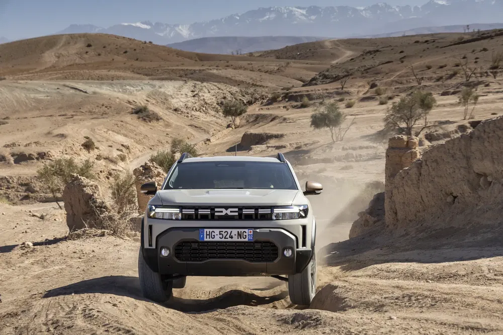 Dacia SUV rijdt op een stoffige woestijnweg met bergen op de achtergrond.
