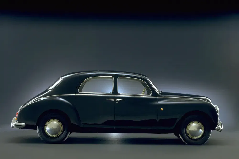 Lancia Aurelia noire des années 1950 sur fond neutre, design élégant et courbé.