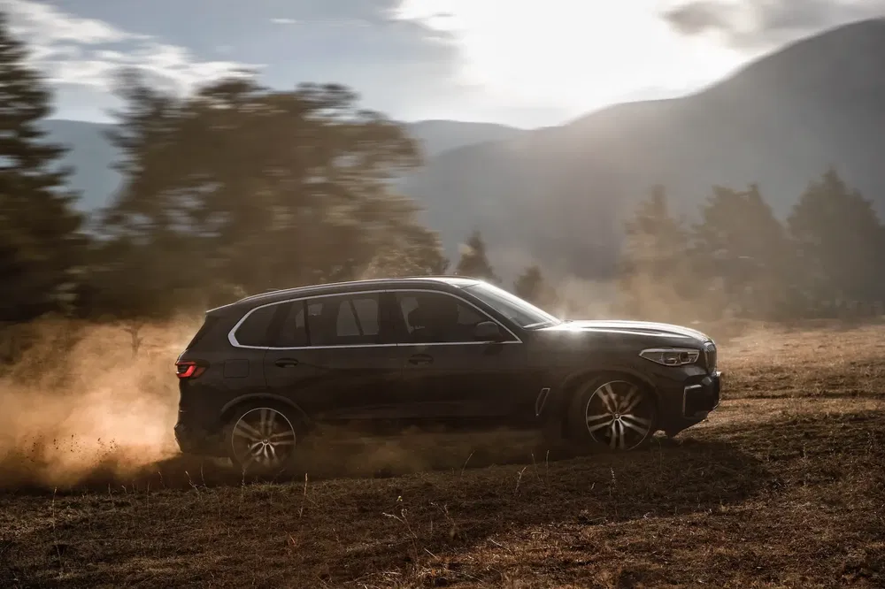 BMW X5 roulant sur un chemin poussiéreux au coucher du soleil, offrant une conduite dynamique.