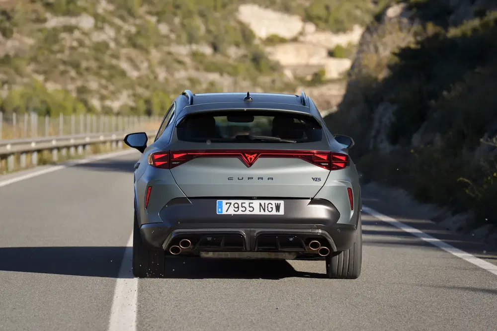 Cupra VZ5 roulant sur une route de montagne, vu de l'arrière, design sportif distinctif.